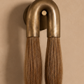 A rustic wall-mounted sconce with two vertical brush-like handles in brown wood, flared with antique brass metal caps, and ending in frosted white glass shades, set against a warm beige textured wall.